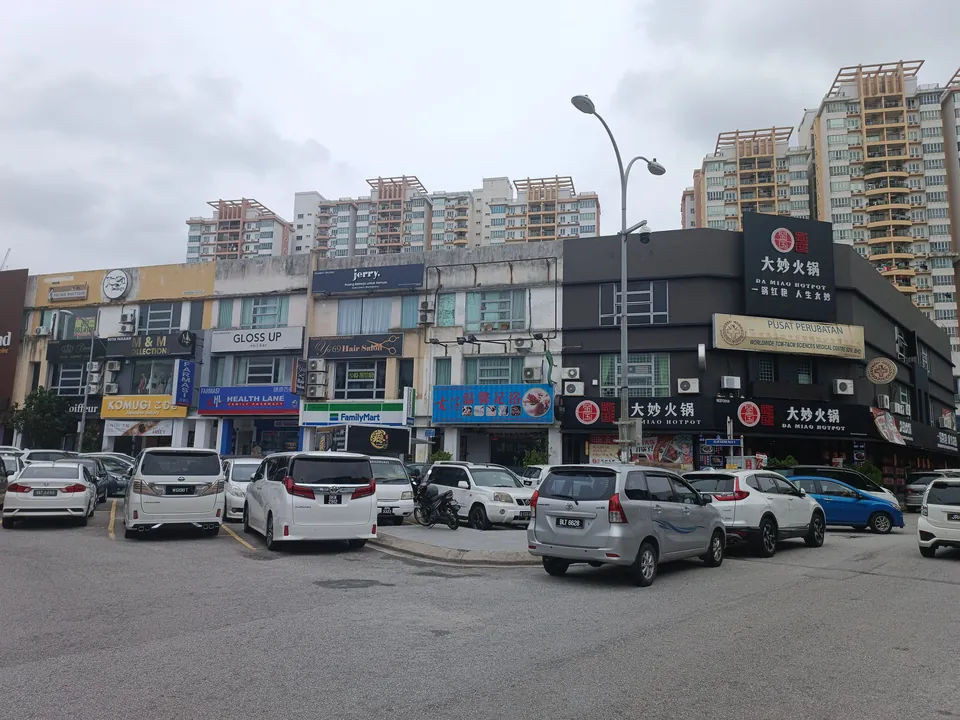 A row of shoplots with a hotpot restaurant sign, a convenience store and a clinic, cars parked in front